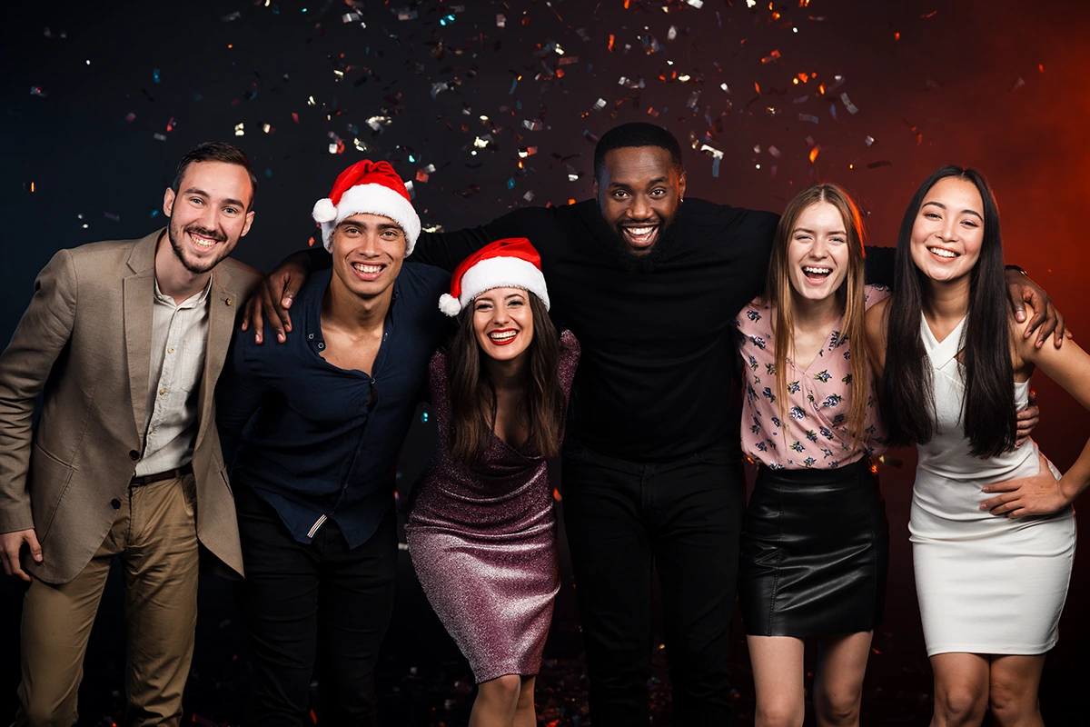 Colleagues in festive dress posing together under confetti at a holiday party