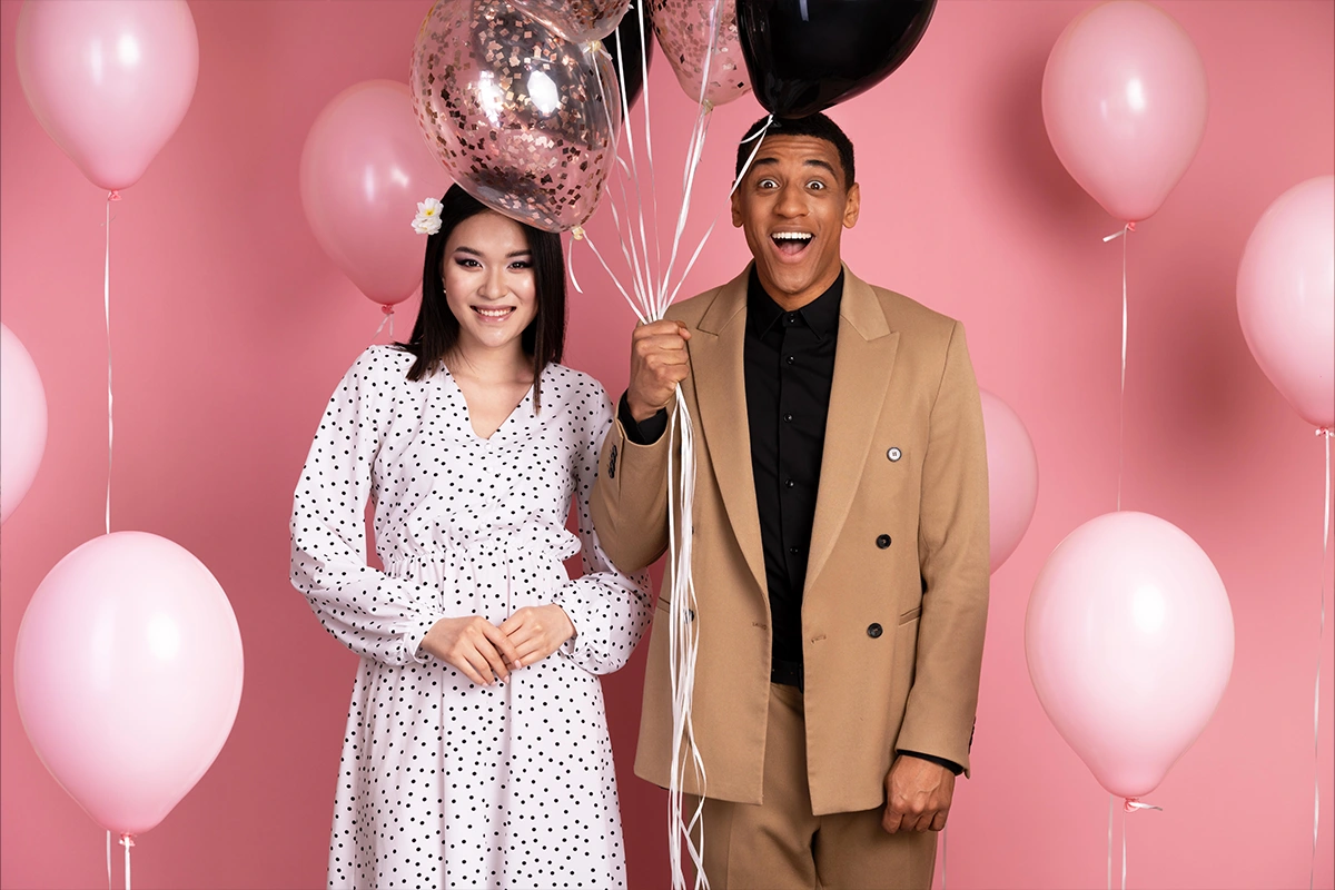 Two guests holding pink and rose gold balloons against a pink backdrop