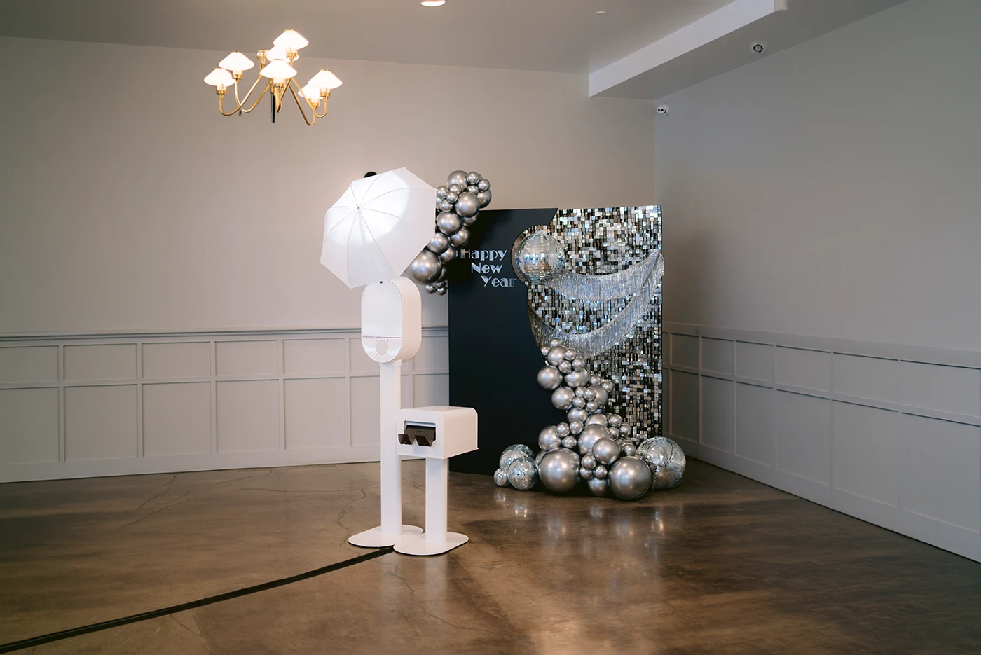 A white photo booth beside a silver sequin backdrop with disco balls and a balloon garland
